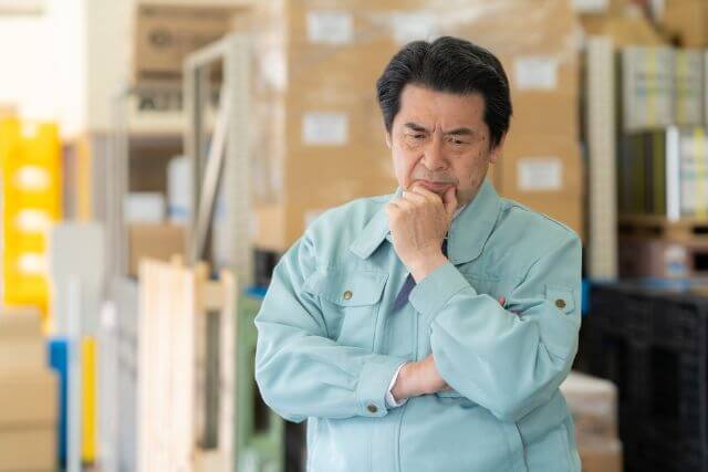 倉庫内で考える作業着の男性